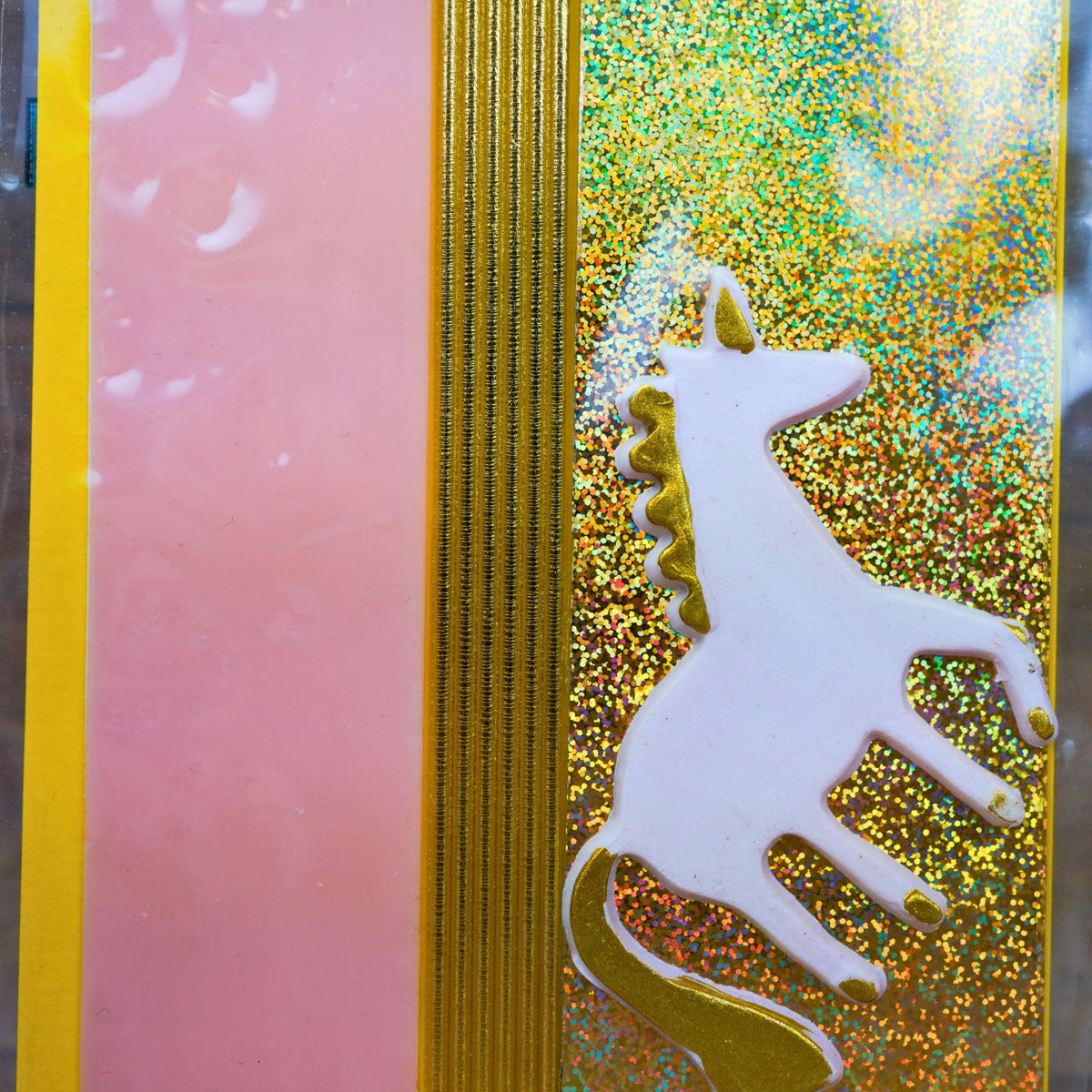 Nahaufnahme weißes Einhorn aus Wachs mit goldener Mähne auf Glitzer-Wachsplatte