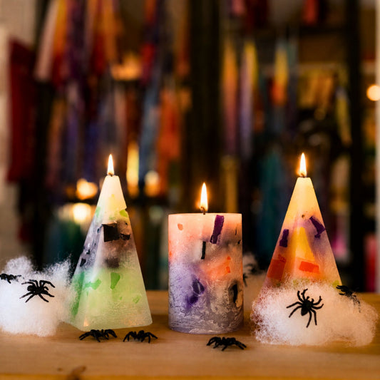 Drei brennende Halloween-Kerzen mit Spinnweben und Deko-Spinnen auf Holztisch