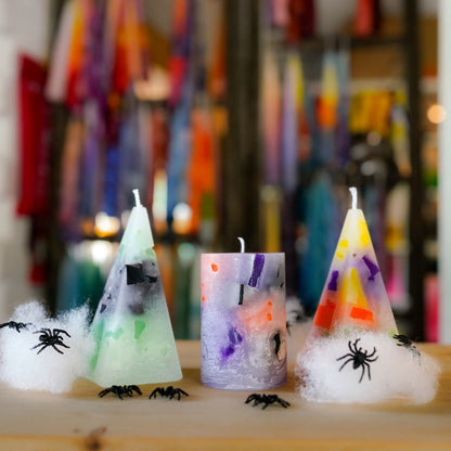 Zwei Pyramidenkerzen und eine Zylinderkerze in Halloween-Farben mit Spinnendeko
