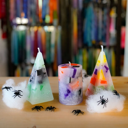 Nahaufnahme dreier Halloween-Kerzen mit bunten Wachswuerfeln und Kunstspinnweben