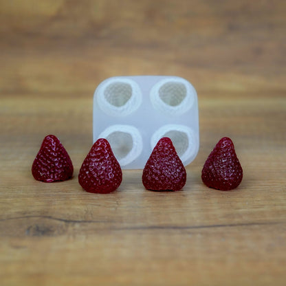 Quadratische Silikonform mit 4 Beeren-Mulden und vier dunkelrot gegossenen Wachserdbeeren